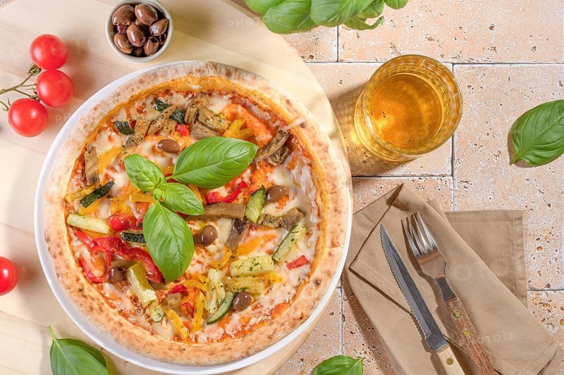 A vibrant vegetarian pizza topped with zucchini, eggplant, peppers, and olives, garnished with fresh basil leaves. Perfect for a healthy and delicious meal