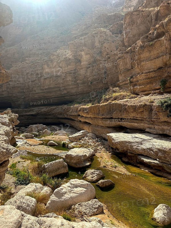 Sunlit view of Wadi Ash Shab, showcasing a picturesque natural oasis surrounded by rugged cliffs and calm water pools in Oman, ideal for nature and travel themes