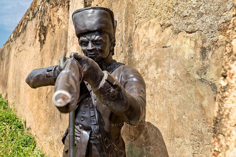 Bronze statue of an aimless soldier with a rifle in front of a wall, statue in the historic fortress of Galle in Sri Lanka