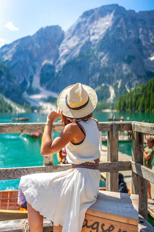 Young woman wearing a straw hat admiring the stunning landscape of lake braies in the italian dolomites during a sunny summer day