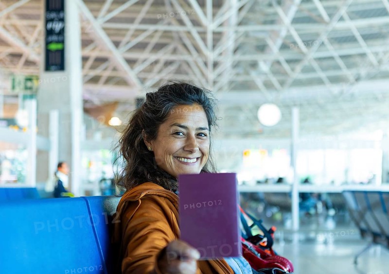 A smiling woman holds her passport in a modern airport terminal She sits on a blue bench, eagerly anticipating her upcoming journey, capturing the essence of travel excitement
