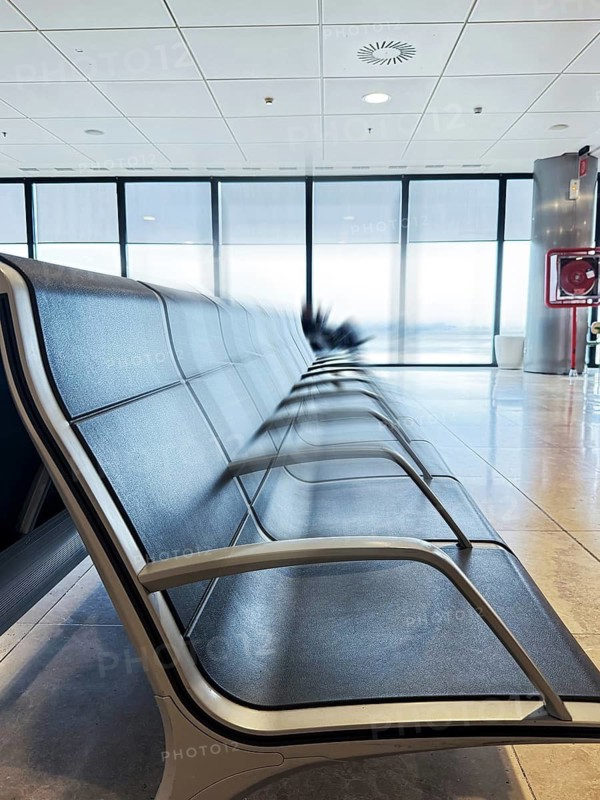 Rows of empty chairs in an airport terminal reflect peacefulness and anticipation. The modern setting, with large windows, invites thoughts of travel and adventure