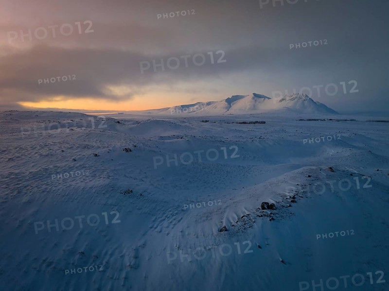 A tranquil winter scene captures Iceland's snow-blanketed land under a vast sky at dusk. Subtle light graces the icy expanse, evoking isolation and pristine beauty