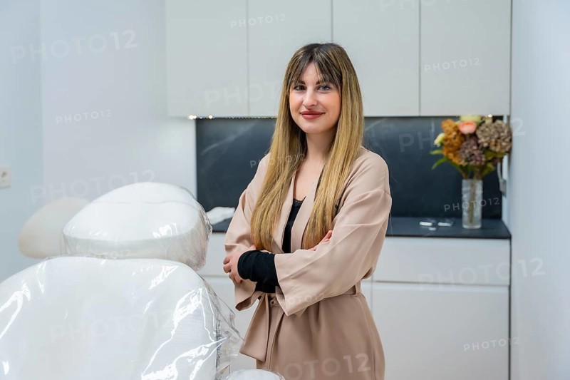 Professional female specialist standing with arms crossed, smiling at the camera in a modern, clean aesthetic center, ready to provide cosmetology and wellness services