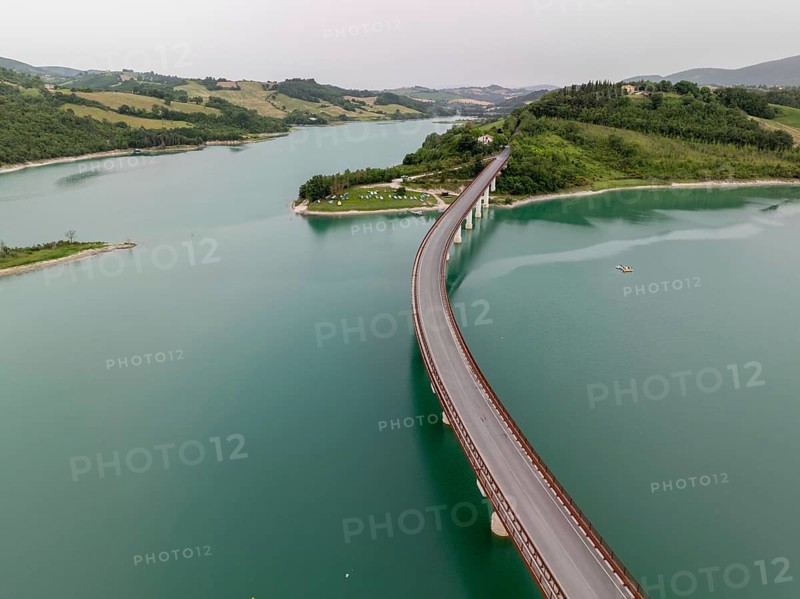 The serene beauty of Lake Castreccioni in Italy. The aerial view highlights its calm waters and the elegant curve of a bridge surrounded by lush green hills