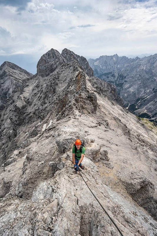 Mountaineer with helmet climbing in a secured climb on the rock, on a narrow rocky ridge, crossing the Jubiläumsgrat, view of Rheintal and Alpspitze, Wetterstein range, Bavaria, Germany
