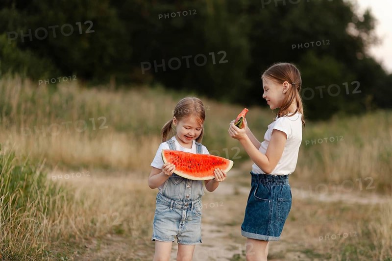 Two young children delight in juicy watermelon slices outdoors during a sunny summer day. Their playful expressions capture the joy of carefree childhood moments