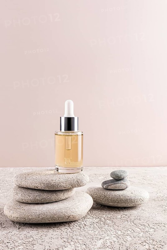 A minimalist composition with a glass dropper bottle of beauty serum atop stacked zen stones, set against a soft pastel background Perfect for skincare and wellness themes