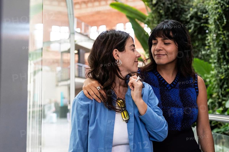 A multiethnic lesbian couple embraces while enjoying a moment together outdoors. Capturing the essence of love and pride, their smiles reflect warmth and connection