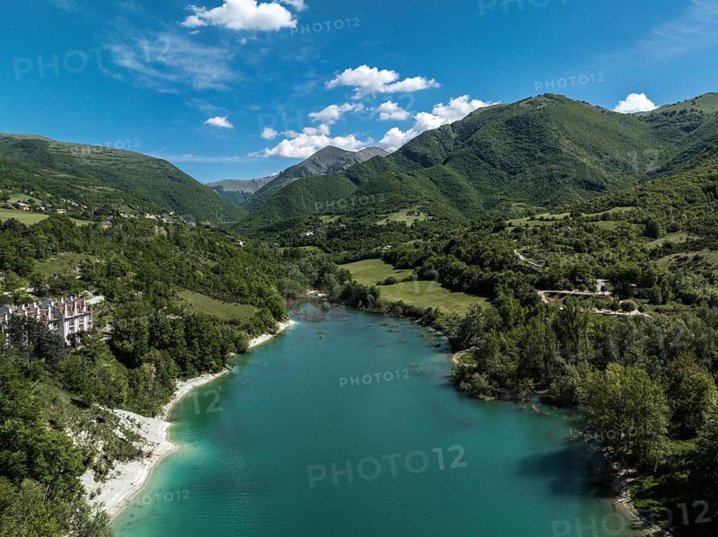 Aerial view of Lago di Fiastra in Italy, featuring turquoise waters, lush green hills, and clear blue skies, creating a serene and picturesque landscape