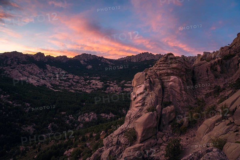 Stunning sunset over the rugged rock formations of Pedriza in the Sierra de Guadarrama, near Madrid. The sky is painted with vibrant hues of orange and pink