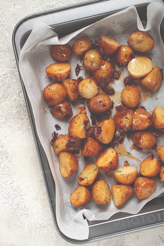 Freshly roasted potatoes golden brown and crispy, seasoned with herbs, resting on parchment paper in a baking tray, ready to serve as a delicious side dish.