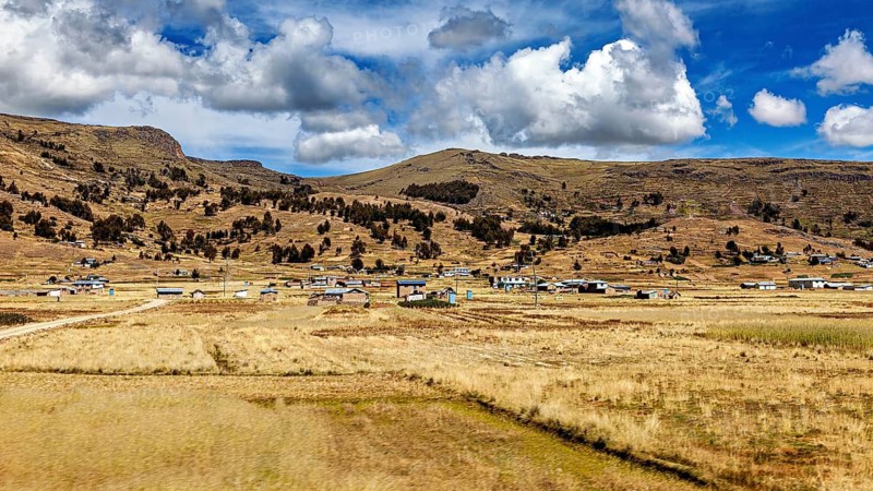 Rural scene with scattered houses in front of mountains under a dramatic sky, The villages and countryside near Puno in Peru