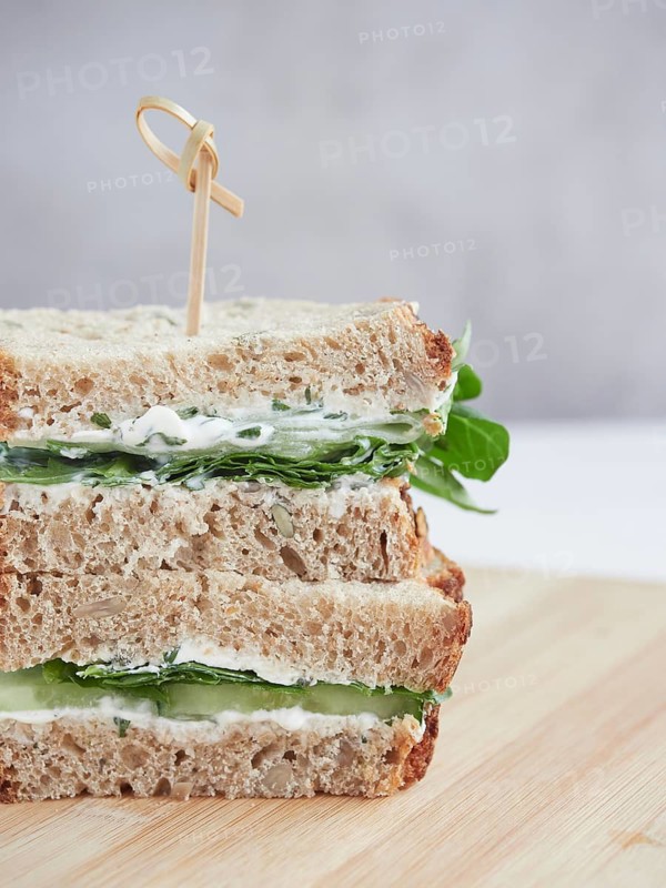 Close up view of cucumber and green spinach sandwich, cut in half and stacked, topped with a bamboo stick