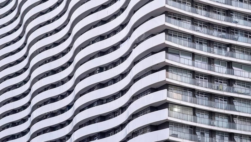 The wavy facade of a modern high-rise building in an urban environment. The repetitive pattern of balconies and windows creates a striking visual effect, emphasizing contemporary architecture's beauty