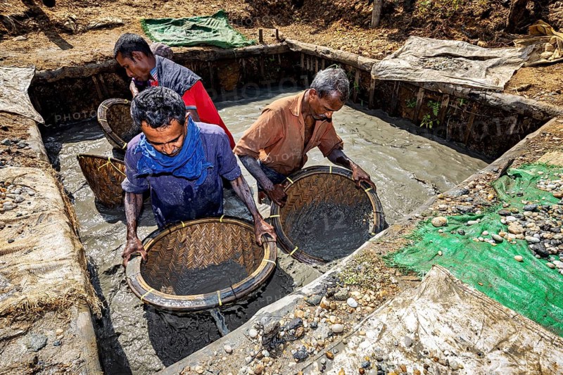 Group of men work together to filter raw materials from a pool of water with baskets, the sapphire and gemstone mines at Ratnapura in Sri Lanka