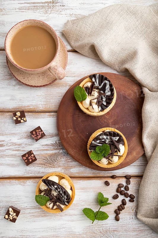 Sweet tartlets with chocolate and cheese cream with cup of coffee on a white wooden background and linen textile. top view, flat lay, close up