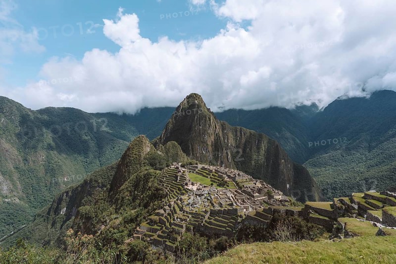 Stunning view of the iconic Machu Picchu ruins set against a backdrop of lush green mountains in Peru. The ancient Incan city is seen under bright, clear skies