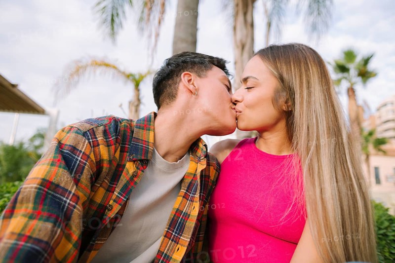 A joyful lesbian couple shares a loving kiss outdoors, surrounded by lush greenery. Their happiness and connection embody pride, diversity, and equality in relationship