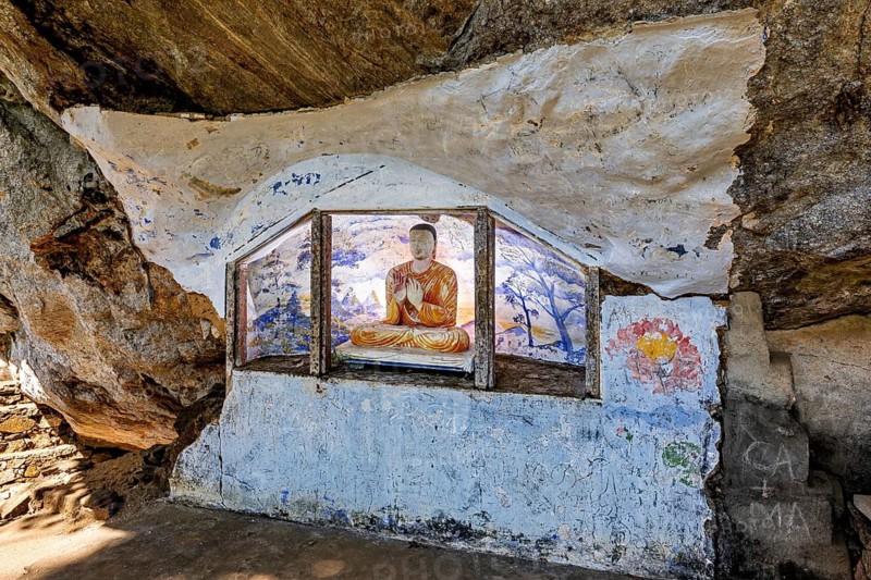 Buddha statue in a small altar in a cave wall surrounded by rock paintings, The Batadombalena cave temple near Ratnapura in Sri Lanka
