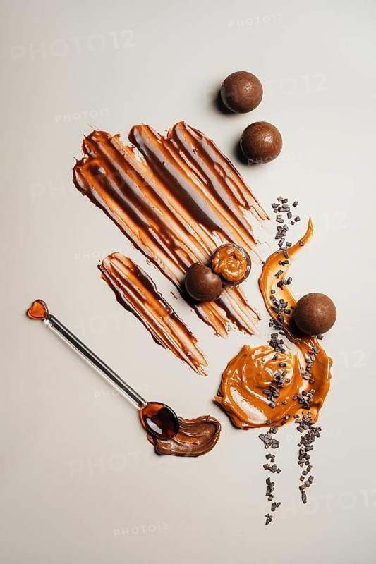 Chocolate balls on a cream surface. A decorative swirl of caramel adds a sweet touch, with cocoa nibs scattered, creating a delightful visual treat