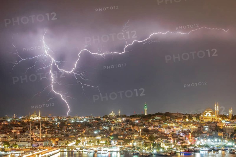 A stunning long-exposure photograph featuring a vivid display of lightning illuminating the night sky above Istanbul's historical architecture and bustling harbor