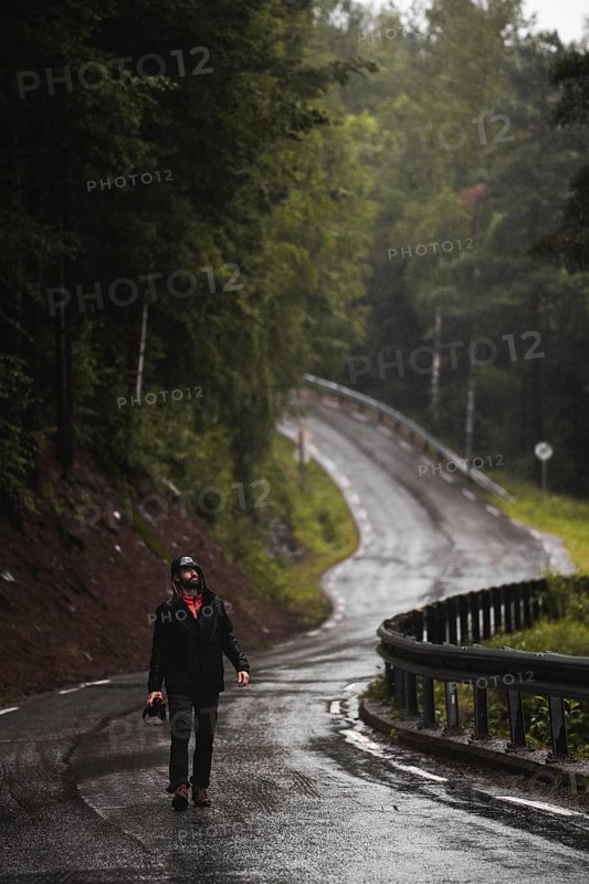 A lone traveler explores a wet, winding road through Norway's lush forest, embodying the spirit of trekking and camping amidst nature's serene beauty