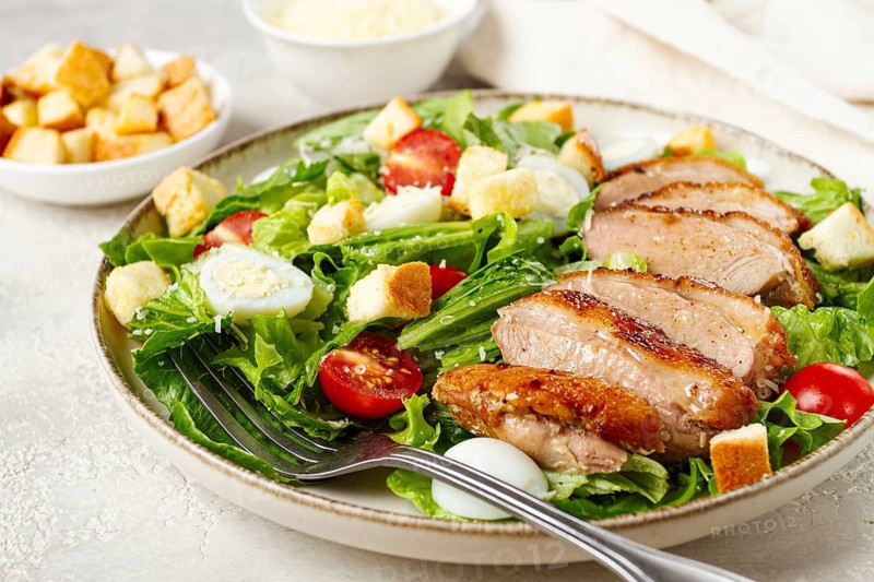 Caesar salad, with duck breast, on a light plate, on a light background, homemade, no people