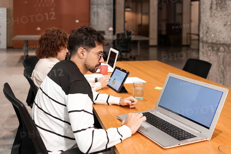 Two coworkers collaborate in a modern office, using laptops and tablets to enhance productivity The workspace emphasizes teamwork, technology, and innovation