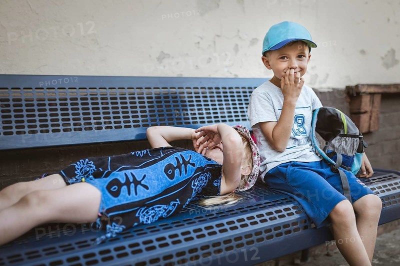Boy and girl waiting on the bench for a train during warm summer day