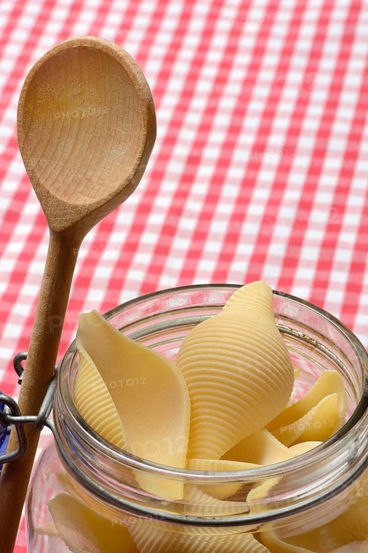 Conchiglione in glass jar with cooking spoon, Italian pasta variety