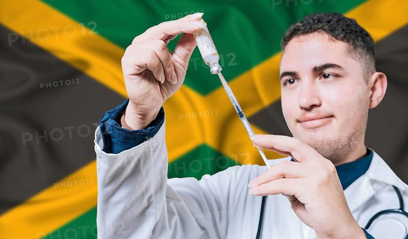 Doctor holding syringe on Jamaica flag background. Medical professional holding syringe with Jamaican flag in the background