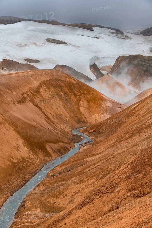 Steaming stream between colourful rhyolite mountains with snowfields, Hveradalir geothermal area, Kerlingarfjöll, Icelandic highlands, Iceland