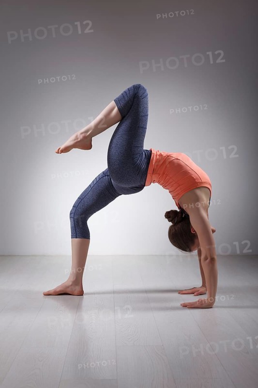 Beautiful sporty fit yogini woman practices yoga asana eka pada chakrasana (or eka pada urdva dhanurasana), one-legged wheel pose (or one-legged upward facing bow) pose in studio