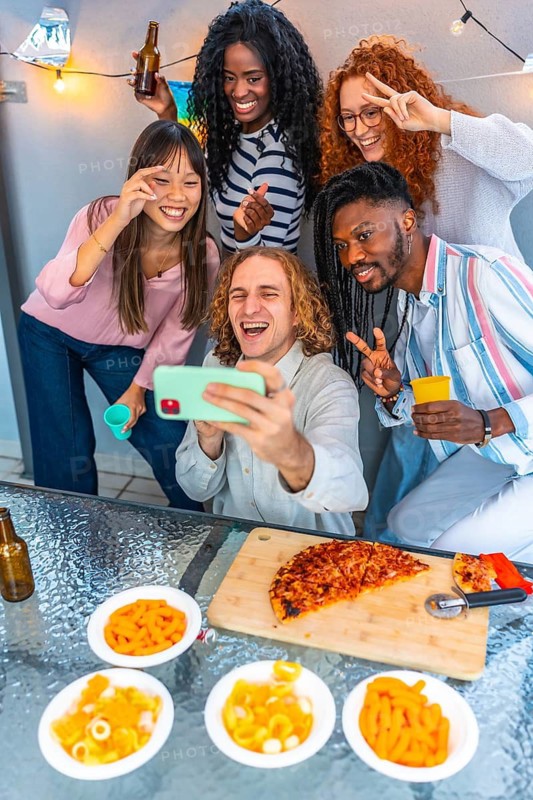 Vertical photo of a group of multi-ethnic happy friends gesturing taking selfie in a rooftop party