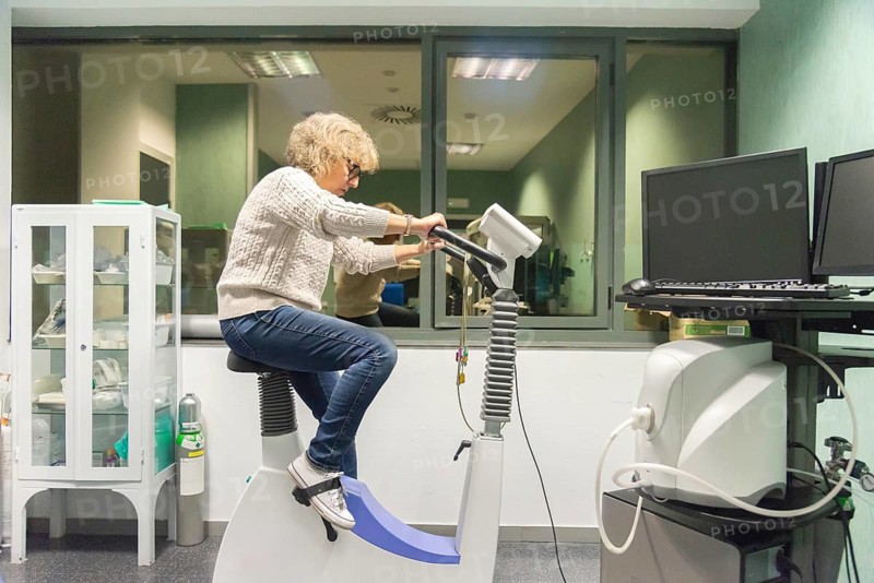 A mature woman performs a cardiovascular stress test in a hospital setting, using specialized equipment to monitor her heart's health