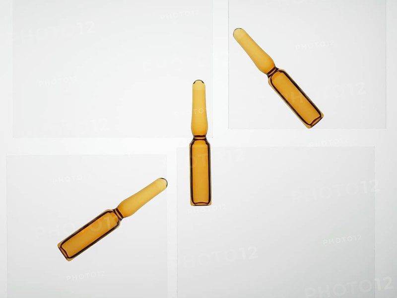 Three amber glass ampoules arranged on a white surface. The clean background and subtle shadows emphasize the simplicity and elegance of the composition of the cosmetic