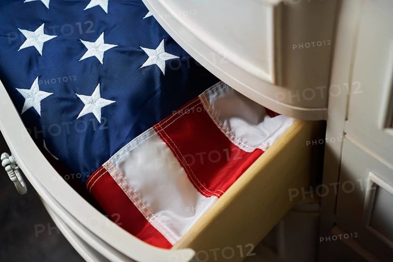 A neatly folded American flag rests inside a wooden drawer, displaying its stars and stripes. This image symbolizes patriotism, heritage, and national pride, evoking a sense of tradition
