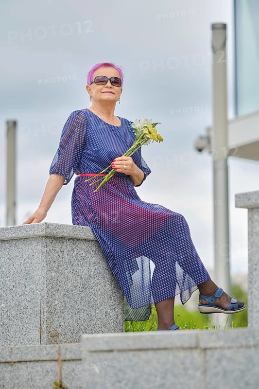 Outdoor portrait of smiling mature woman with short pink hair with spring flowers in hands