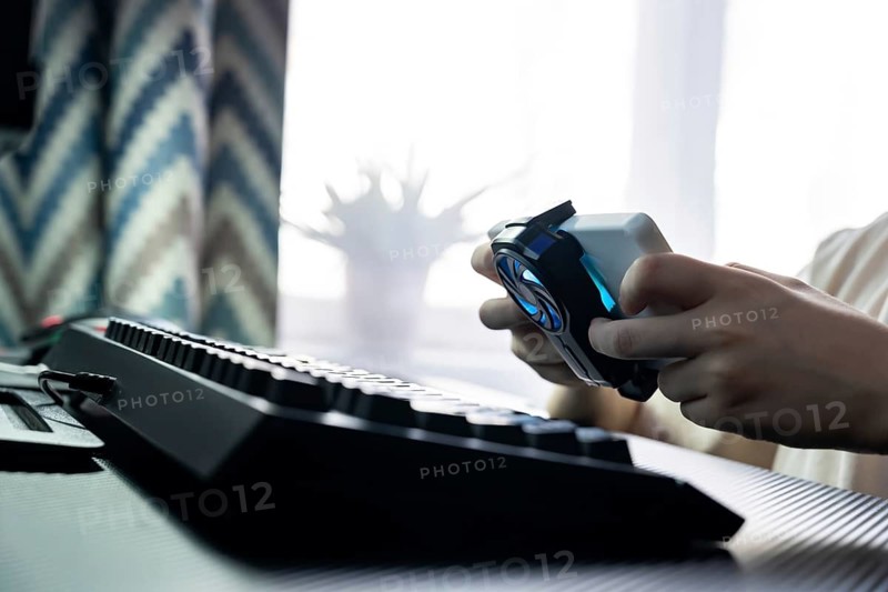 A focused teenage boy holds a gaming controller, engaged in intense gameplay, with a sleek keyboard in view. The gaming theme captures the excitement of technology and youth