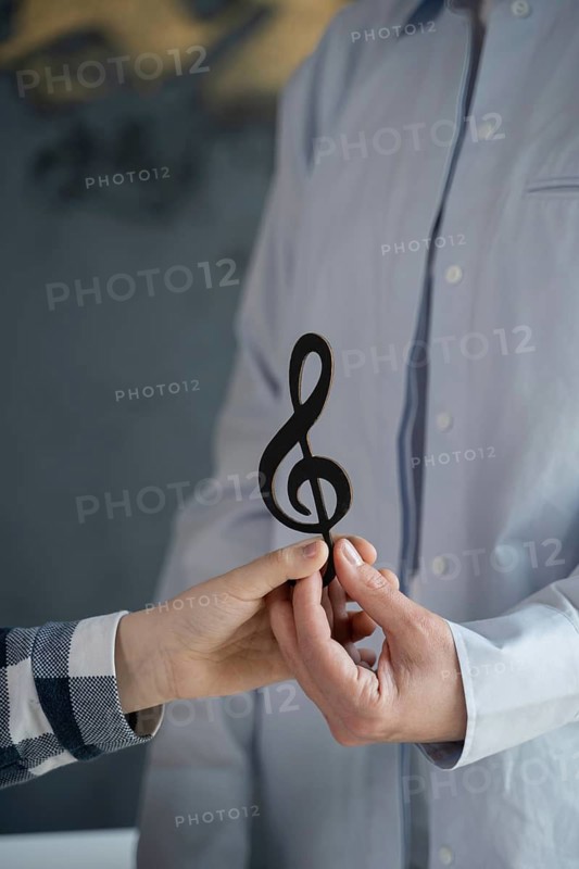 Close-up of two hands holding a wooden treble clef symbol, symbolizing collaboration and creativity in music. Ideal for themes of music, teamwork, and artistic expression