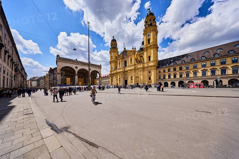 Theatine Church, St. Cajetan and Adelaide, double tower, Italian high Baroque style, Feldherrnhalle building style, classicism style, pedestrian zone, square, street, building renovation, fenced construction site, pedestrians and cyclists as a secondary motif, blue sky, cumulus clouds, Residenzstraße and Theatinerstraße confluence in Odeonsplatz, Munich, state capital, district free city, Bavaria, Germany