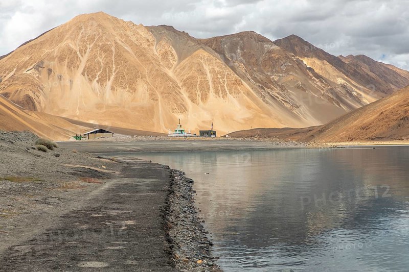 Scenic view of Pangong Tso lake in Ladakh, India, surrounded by the majestic Himalayas with calm waters reflecting the striking mountains under a cloudy sky