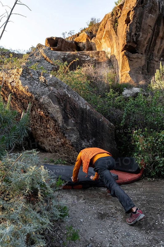 An adventurous climber gears up to tackle a challenging boulder in a picturesque natural setting. Surrounded by greenery, towering rocks create an inspiring outdoor scene