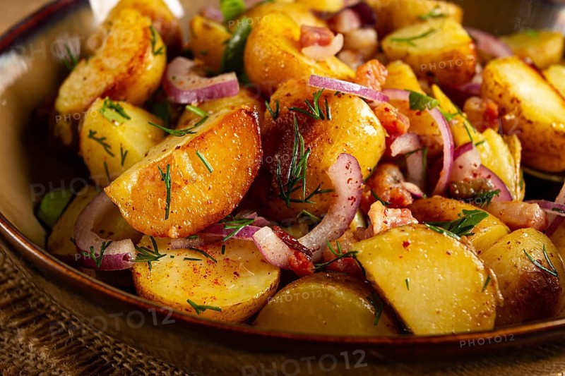 German potato salad with bacon, onions and herbs, plate on a wooden table, rustic style, no people