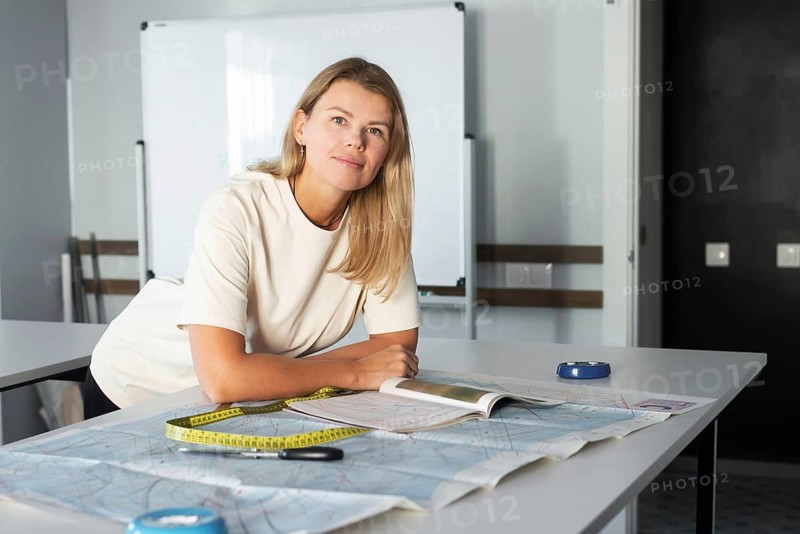 A woman leans over a desk in a sewing studio, surrounded by fabric, scissors, and a measuring tape, planning her next creative sewing project