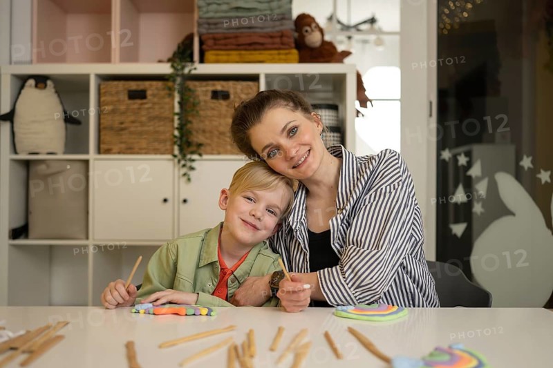 Teacher and student sitting at a table, making crafts with colored clay and sticks, creating a warm and creative home environment