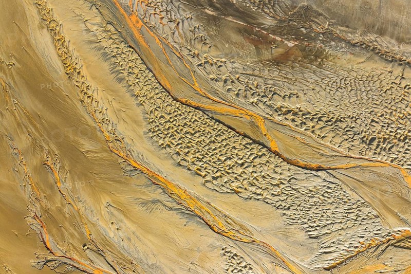 Aerial view captures a textured sand scape, showcasing flowing patterns of earthy tones and striking orange lines. The natural design resembles an abstract painting