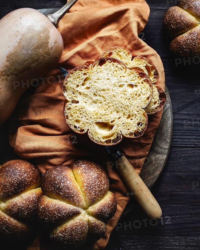 Freshly baked homemade pumpkin bread displayed on a rustic wooden table alongside a butternut squash. The bread golden crust and soft interior evoke cozy autumn vibes