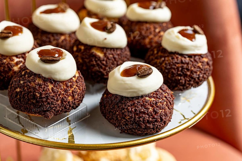 Indulge in these exquisite coffee cream puffs topped with luscious cream and a coffee bean garnish, elegantly presented on a gold finished cake stand, perfect for a gourmet setting